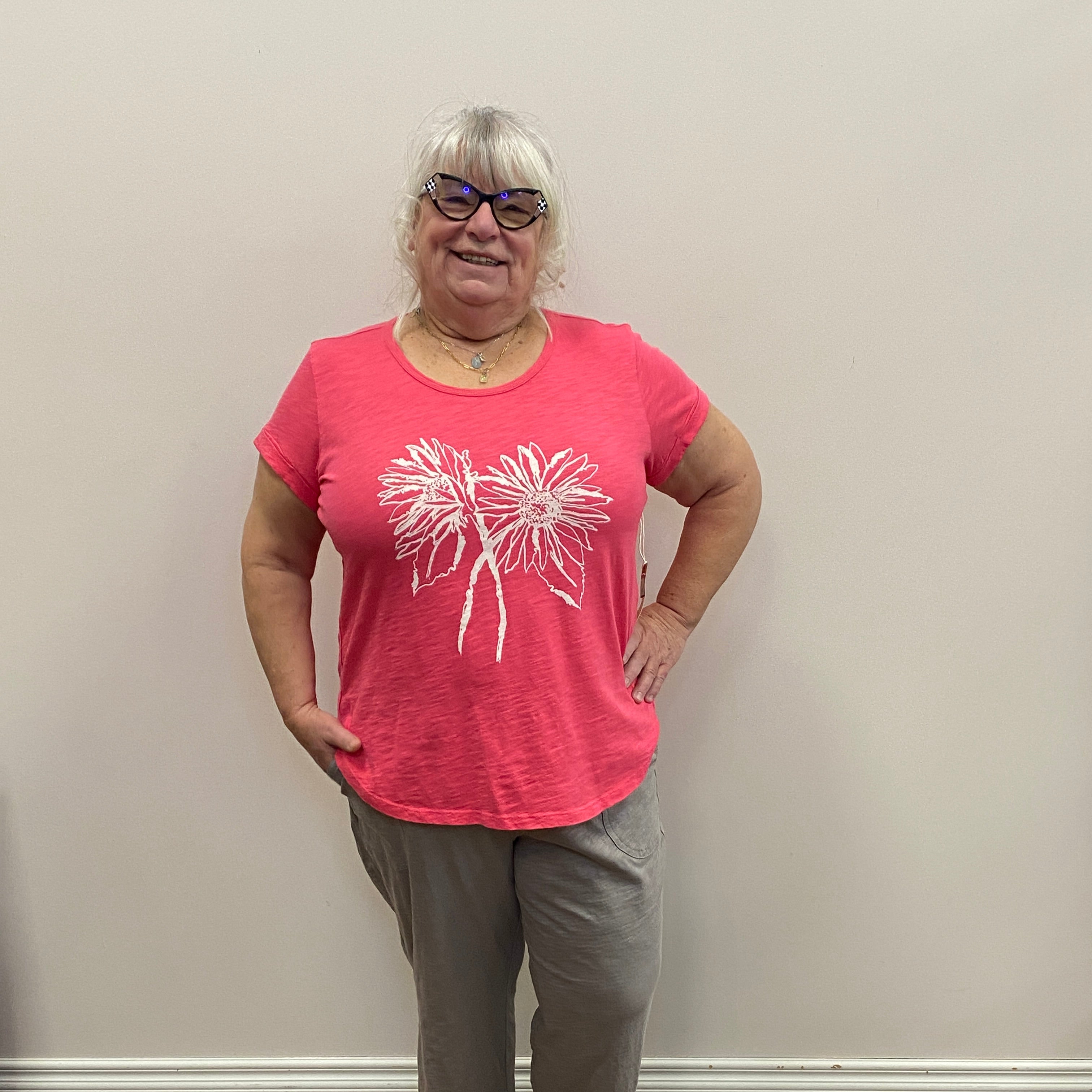 Person wearing a pink t-shirt with a white floral design, standing indoors on a wooden floor.
