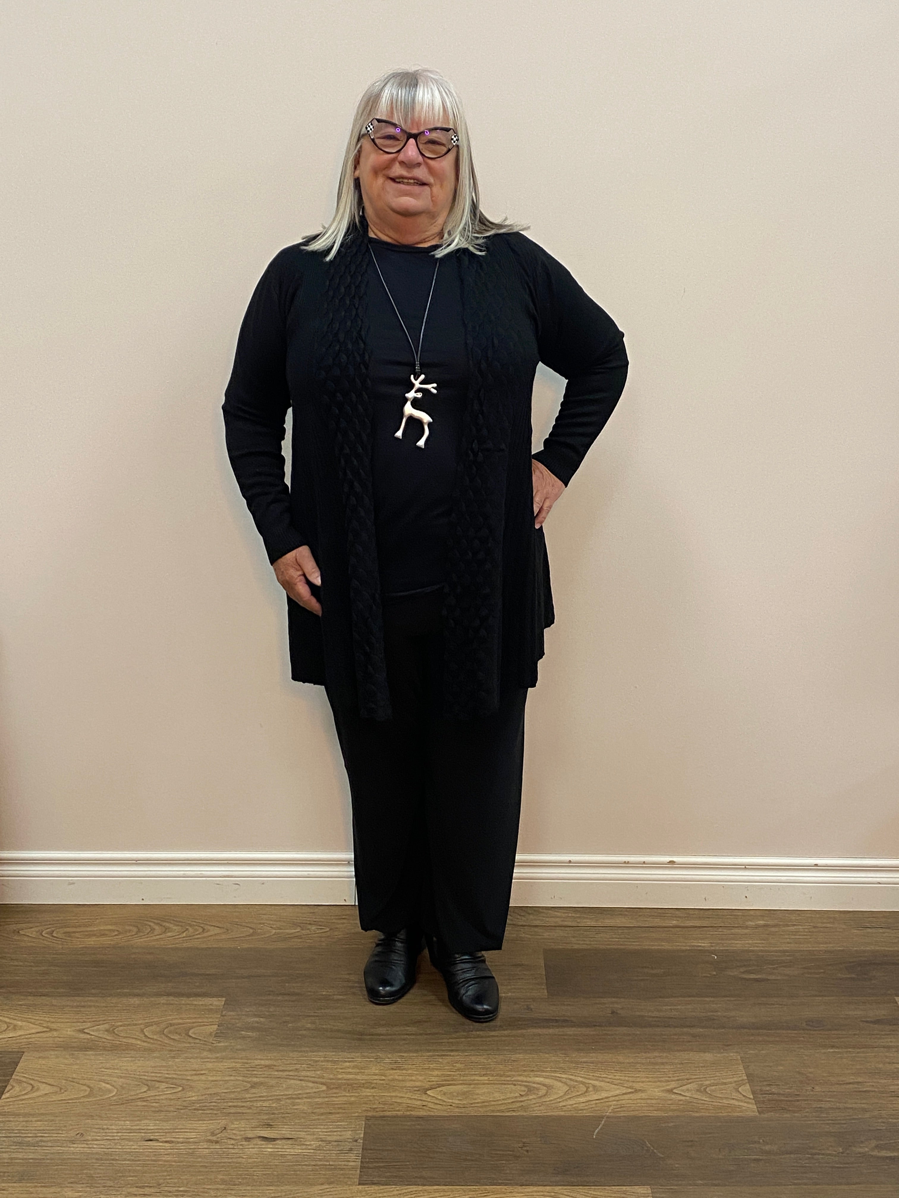 Person wearing a black outfit with a white wall and wooden floor background