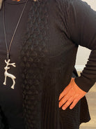 Person wearing a textured black garment with a hand on the fabric, against a neutral background.