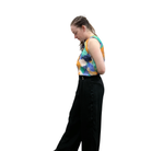 Person wearing a colorful sleeveless top and black pants on a white background