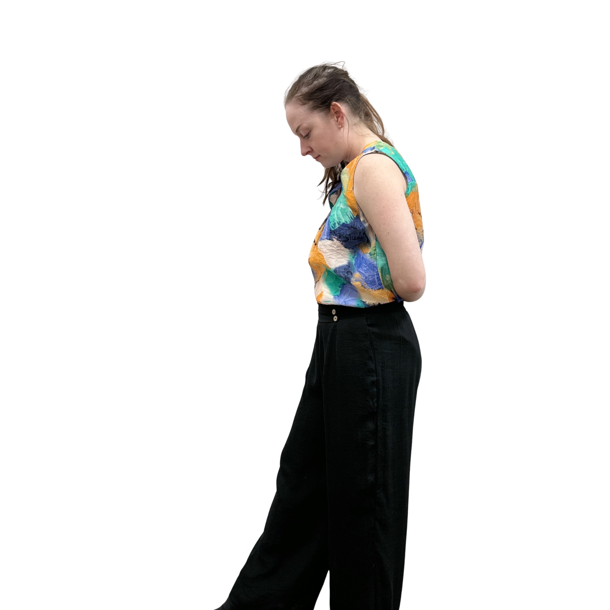 Person wearing a colorful sleeveless top and black pants on a white background