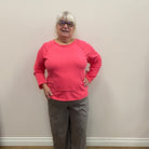 Person wearing a pink sweatshirt and gray pants standing against a white wall.