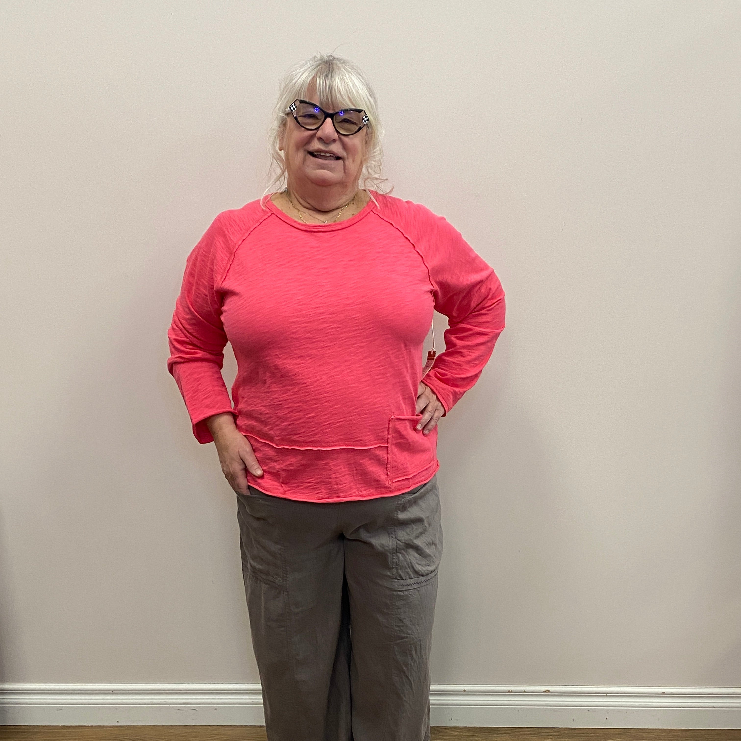 Person wearing a pink sweatshirt and gray pants standing against a white wall.