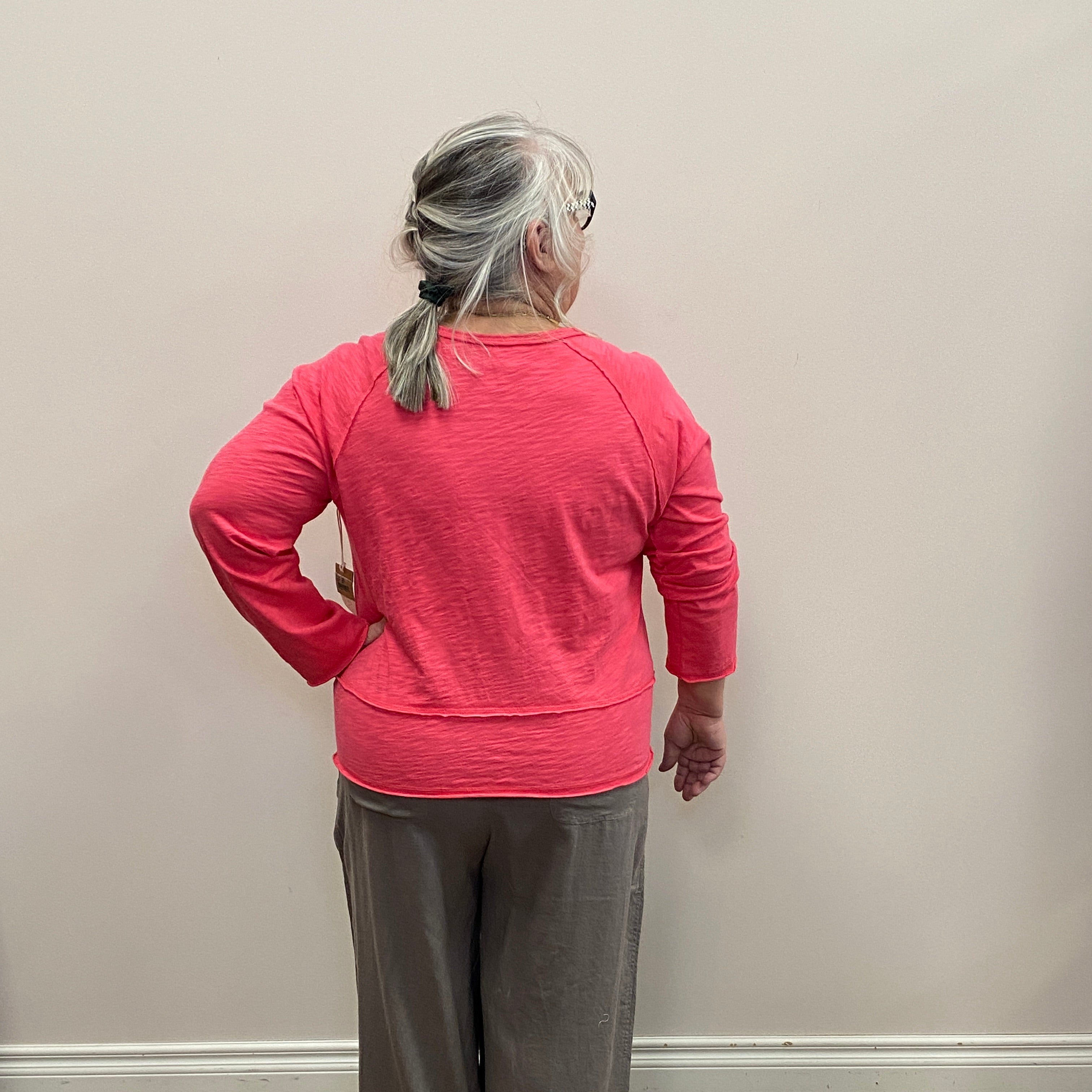 Person wearing a pink sweater and gray pants standing against a white wall.
