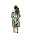 Woman wearing a sleeveless dress with a colorful tropical leaf pattern on a white background