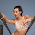 Woman in a beige sports bra and shorts against a blue background