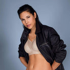 Woman wearing a black leather jacket over a beige bra against a gray background