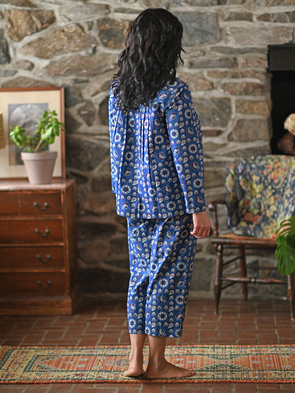 A woman wearing a blue pajama set against a grey wall.