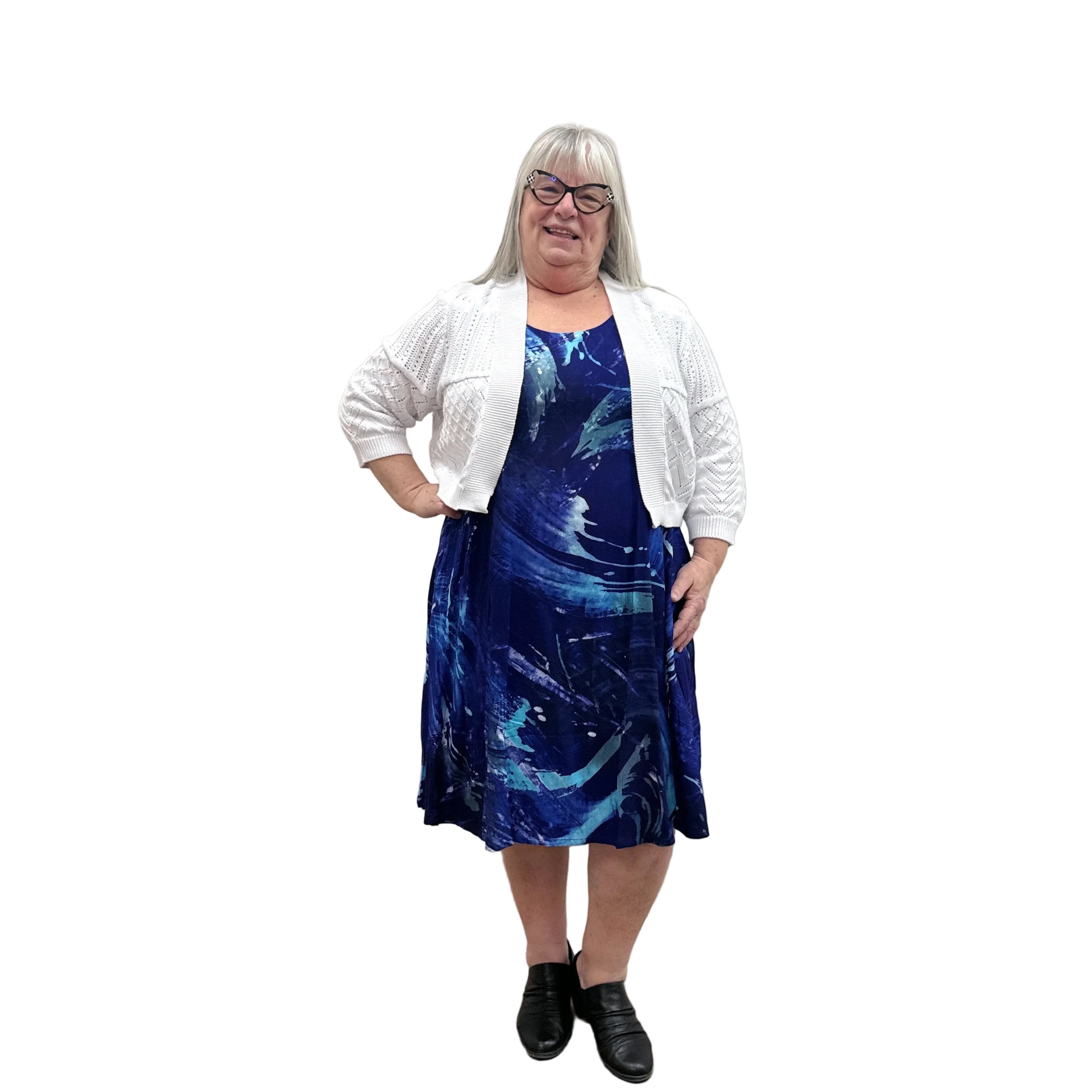 Woman wearing a white Blue Sky Aldi Sweater over a blue patterned dress on white background. 