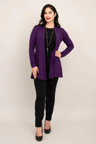 Woman wearing a purple cardigan over a black top and pants on a beige background