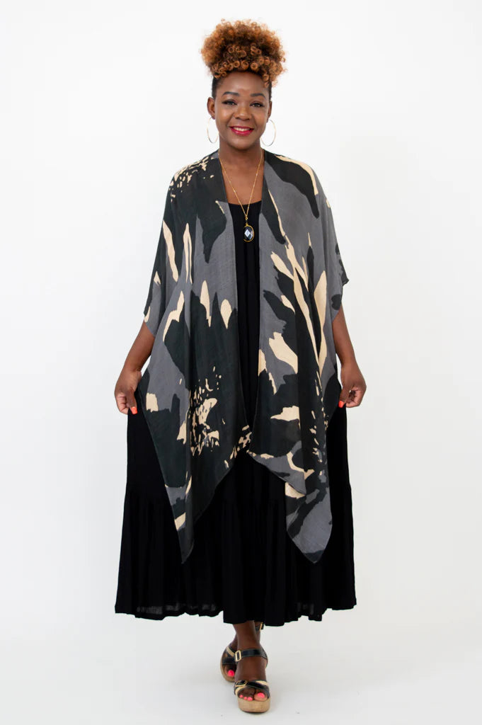 Woman wearing a long, patterned gray and black coat over a black dress on a white background