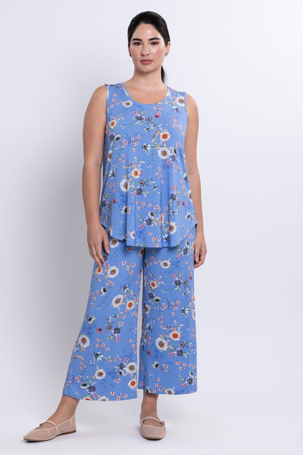Woman wearing a blue floral sleeveless top and wide-leg pants on a white background