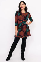 Woman wearing a patterned dress with black leggings and boots on a white background
