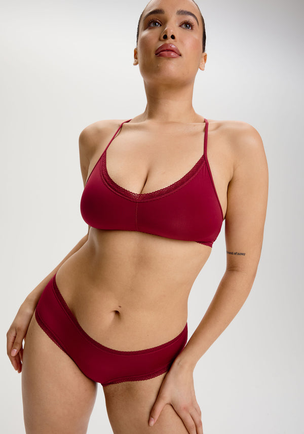 Model wearing the Rosewood Dark Red Hipster Panties in soft microfibre fabric with a low rise and lace trim for a whole body view, paired with a bralette. 