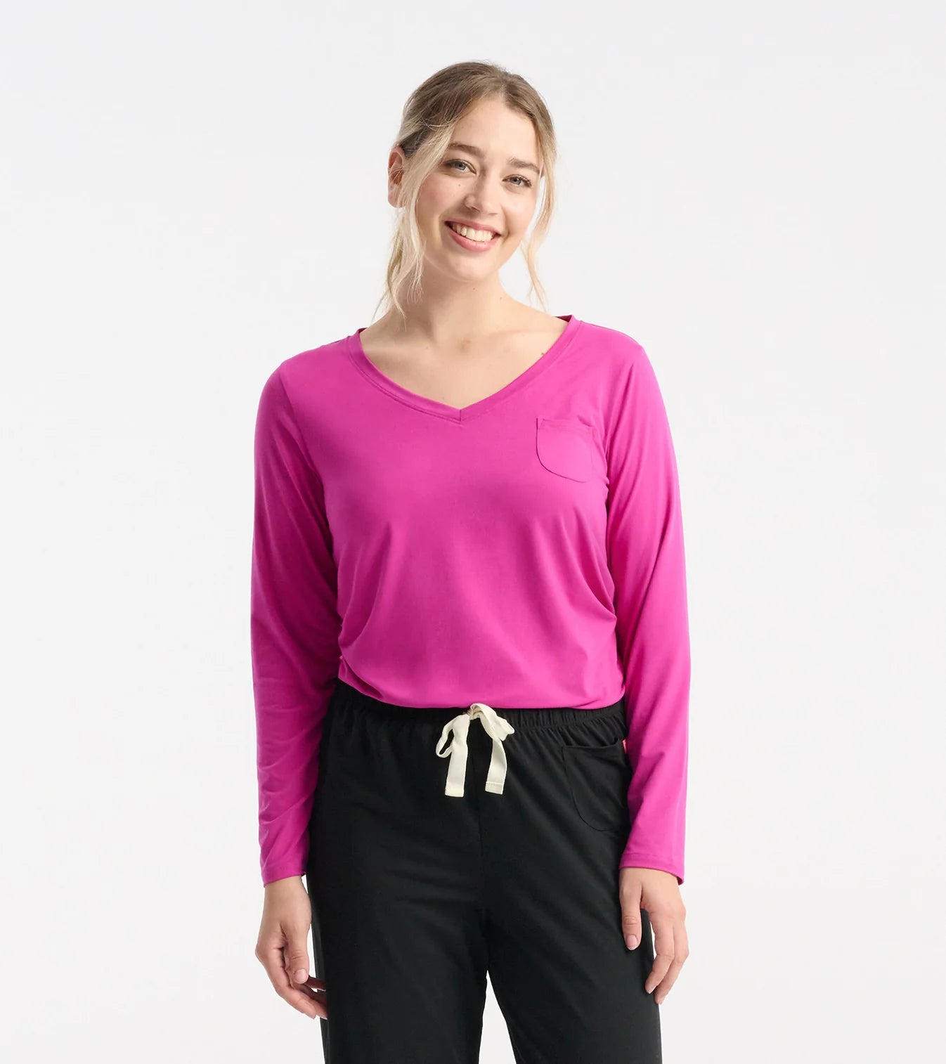 Woman wearing a bright pink long-sleeve shirt and black pants on a white background