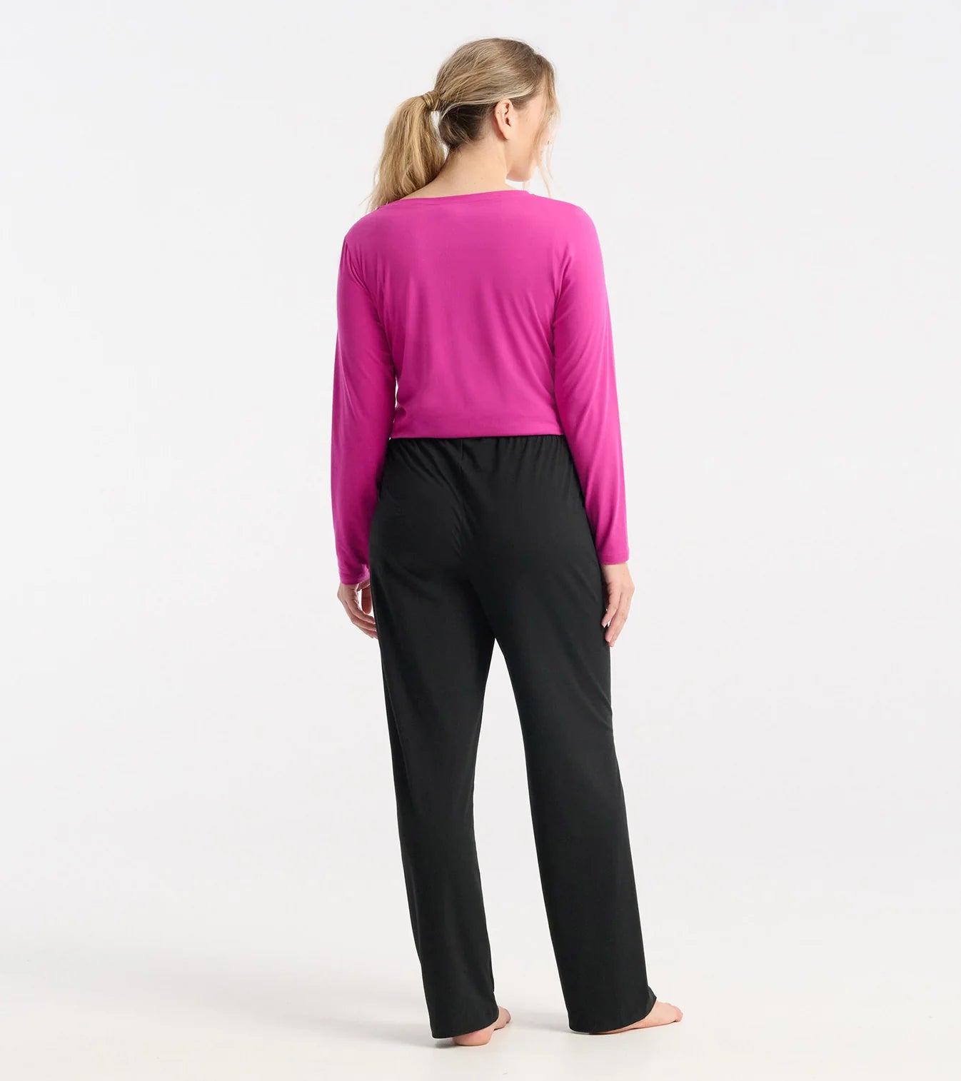 Woman wearing a bright pink long-sleeve top and black pants on a white background