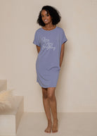 Woman wearing a purple nightshirt with text on it against a neutral background