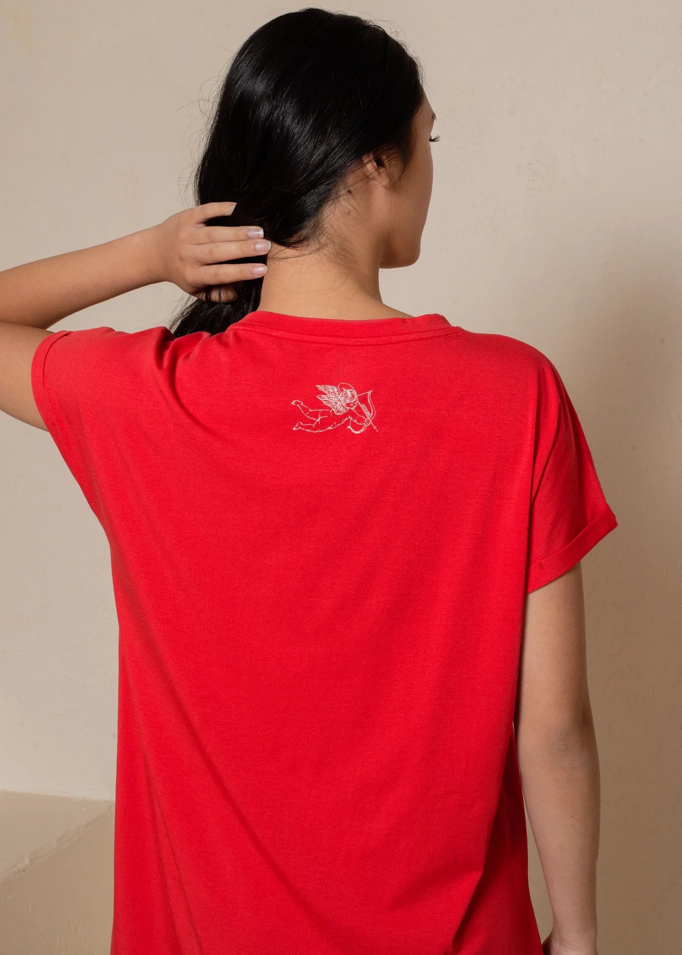 Person wearing a red shirt with a white logo on the back against a beige background