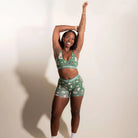 Woman wearing a green bralette and shorts set with visible branding against a plain background