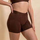 Person wearing brown athletic shorts and bralette on a beige background