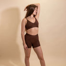 Woman wearing a brown bralette and shorts set against a beige background