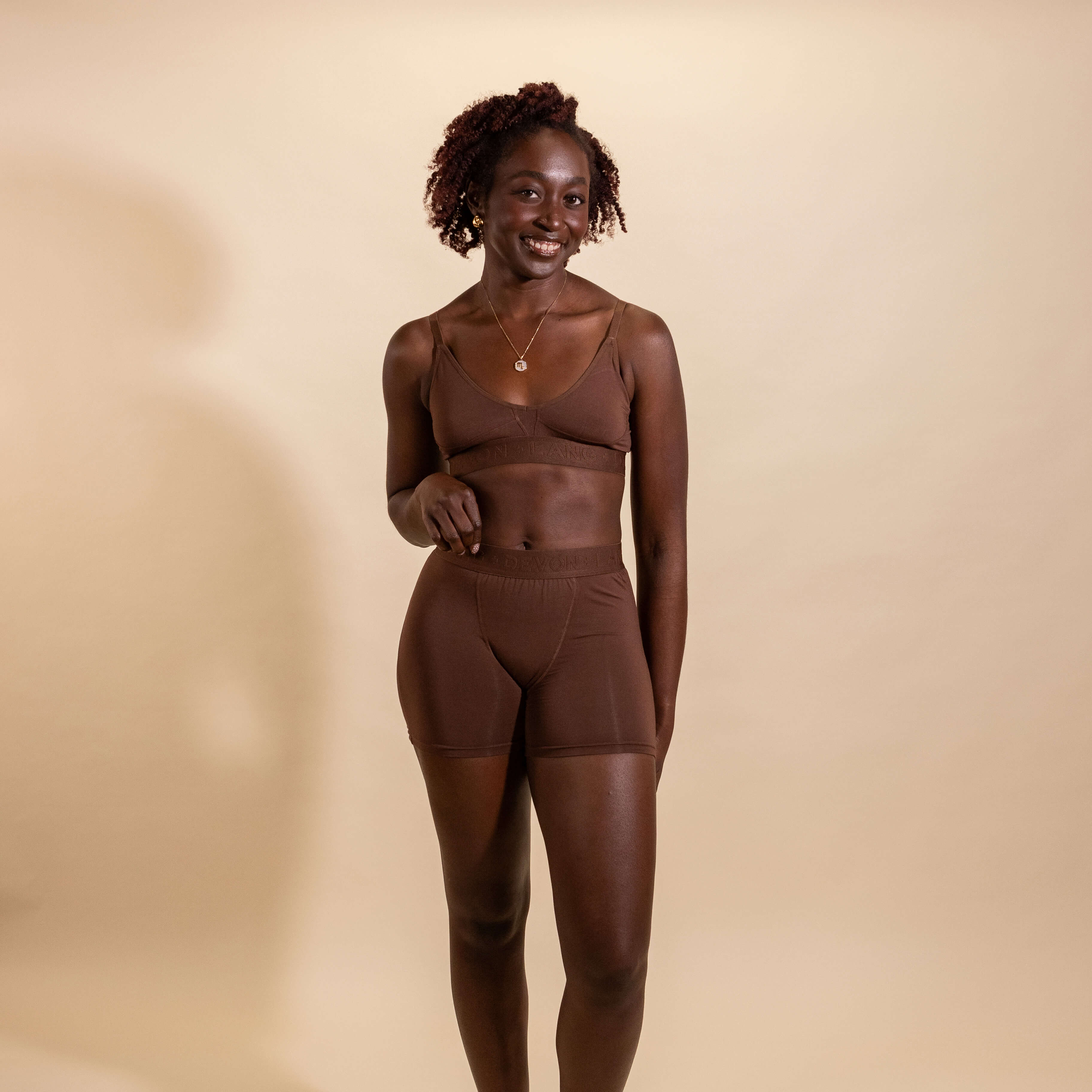Woman wearing a brown bralette and shorts set against a beige background