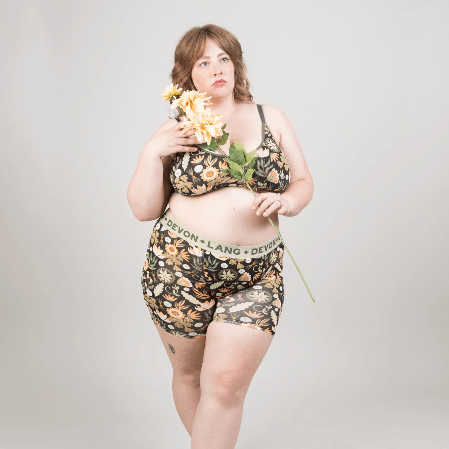 Woman wearing a floral lingerie set holding flowers against a plain background