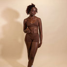 Woman wearing a brown bra and panties set against a beige background