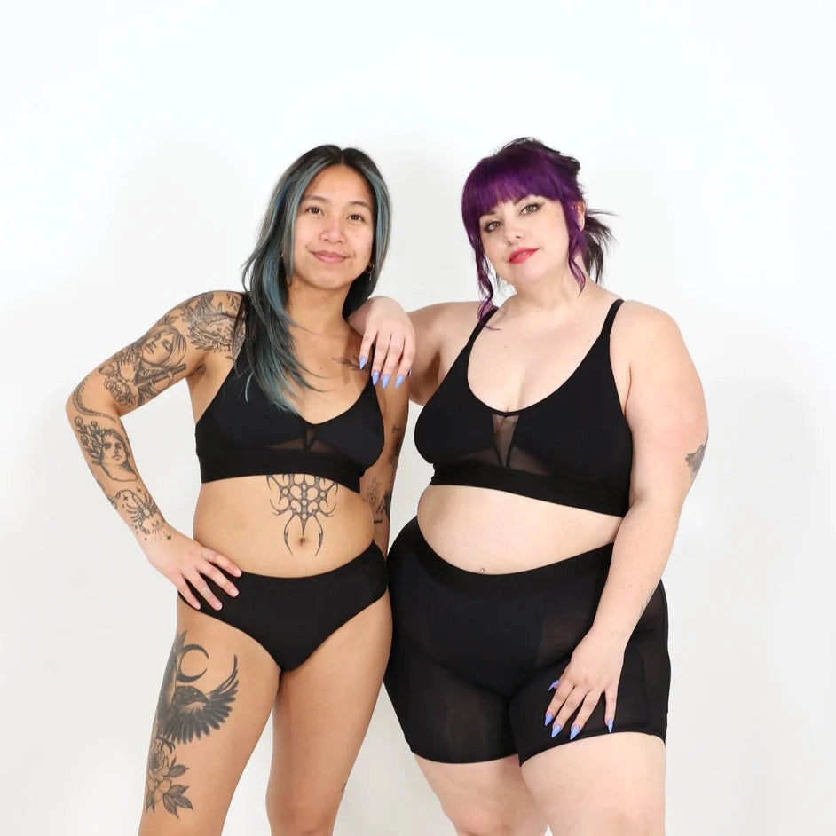 Two women wearing black bra and underwear sets on a white background