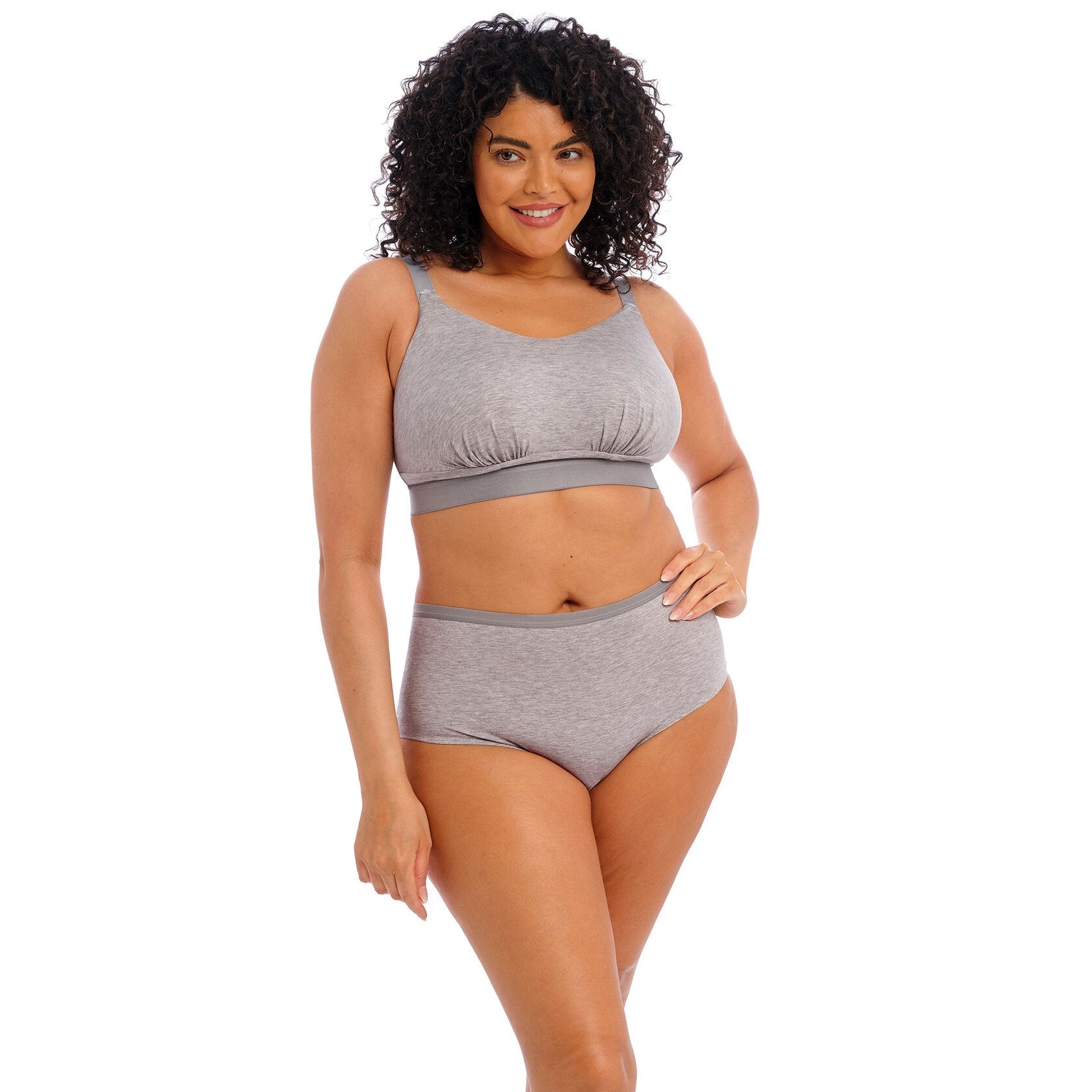 A woman wearing a grey wireless bra and high rise panty against a white back ground. 