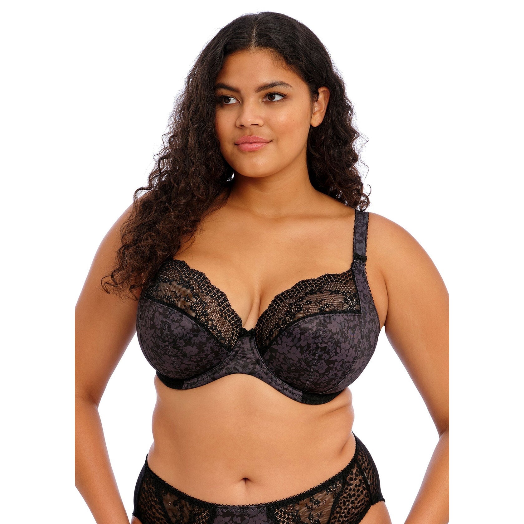 A women wearing a black lace bra and panty set against a white background. 