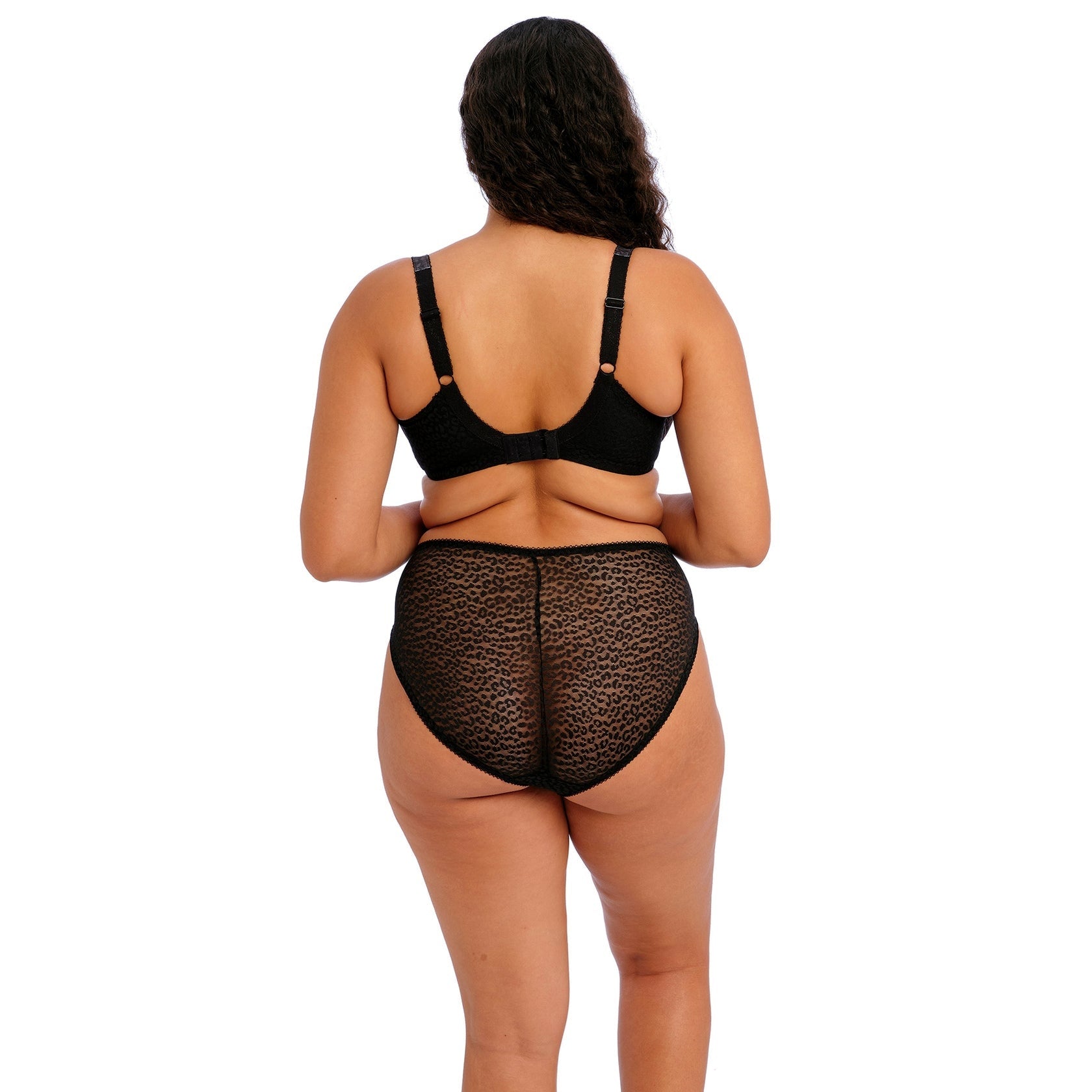 A person wearing a black bra and panty set against a white back ground. 
