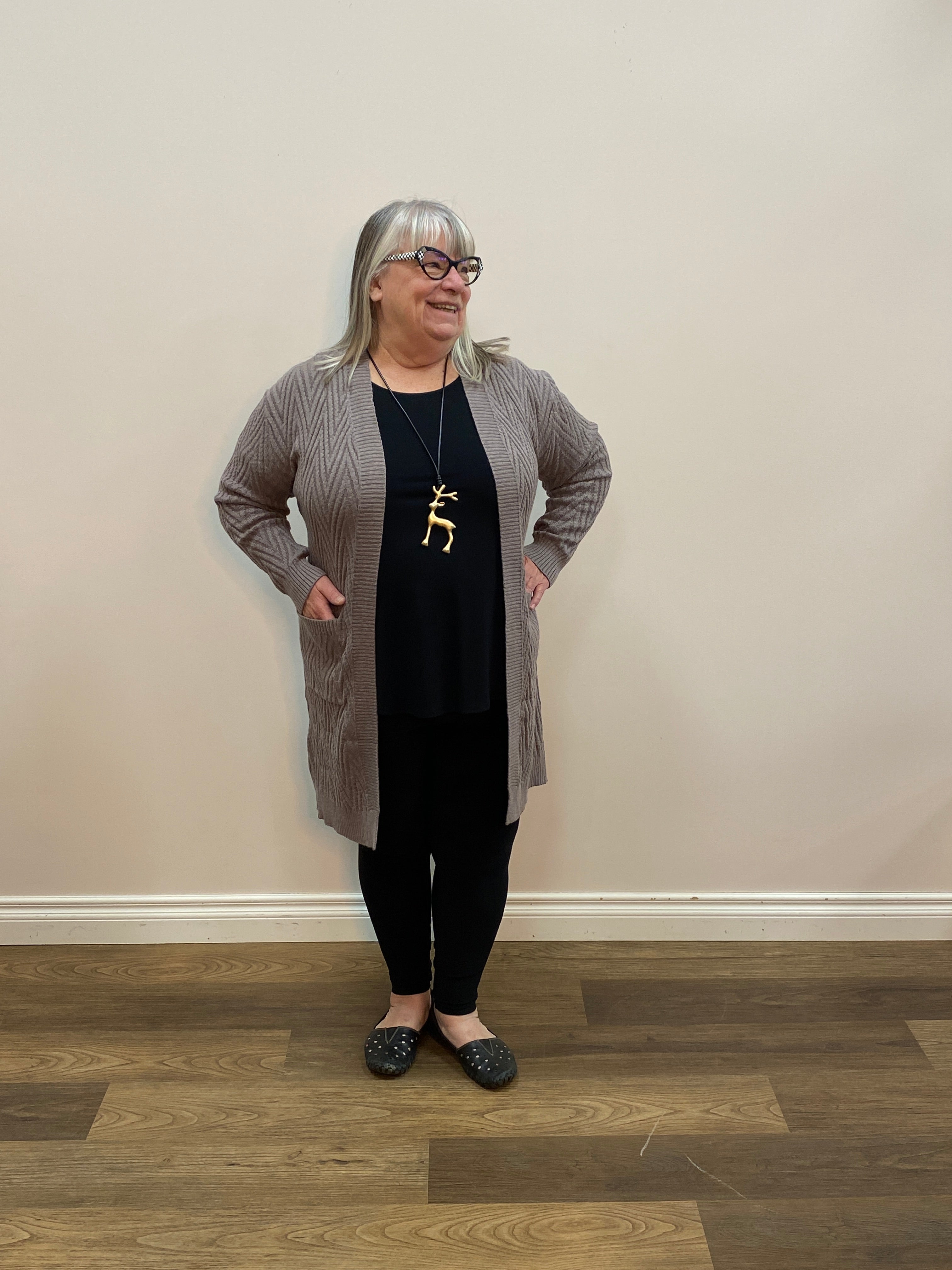 Person standing in a room with wooden flooring and a white wall.
