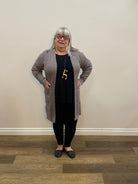 Person wearing a gray sweater and black pants standing on a wooden floor.