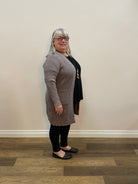 Person standing in a room wearing a grey cardigan with a neutral wall and wooden floor.