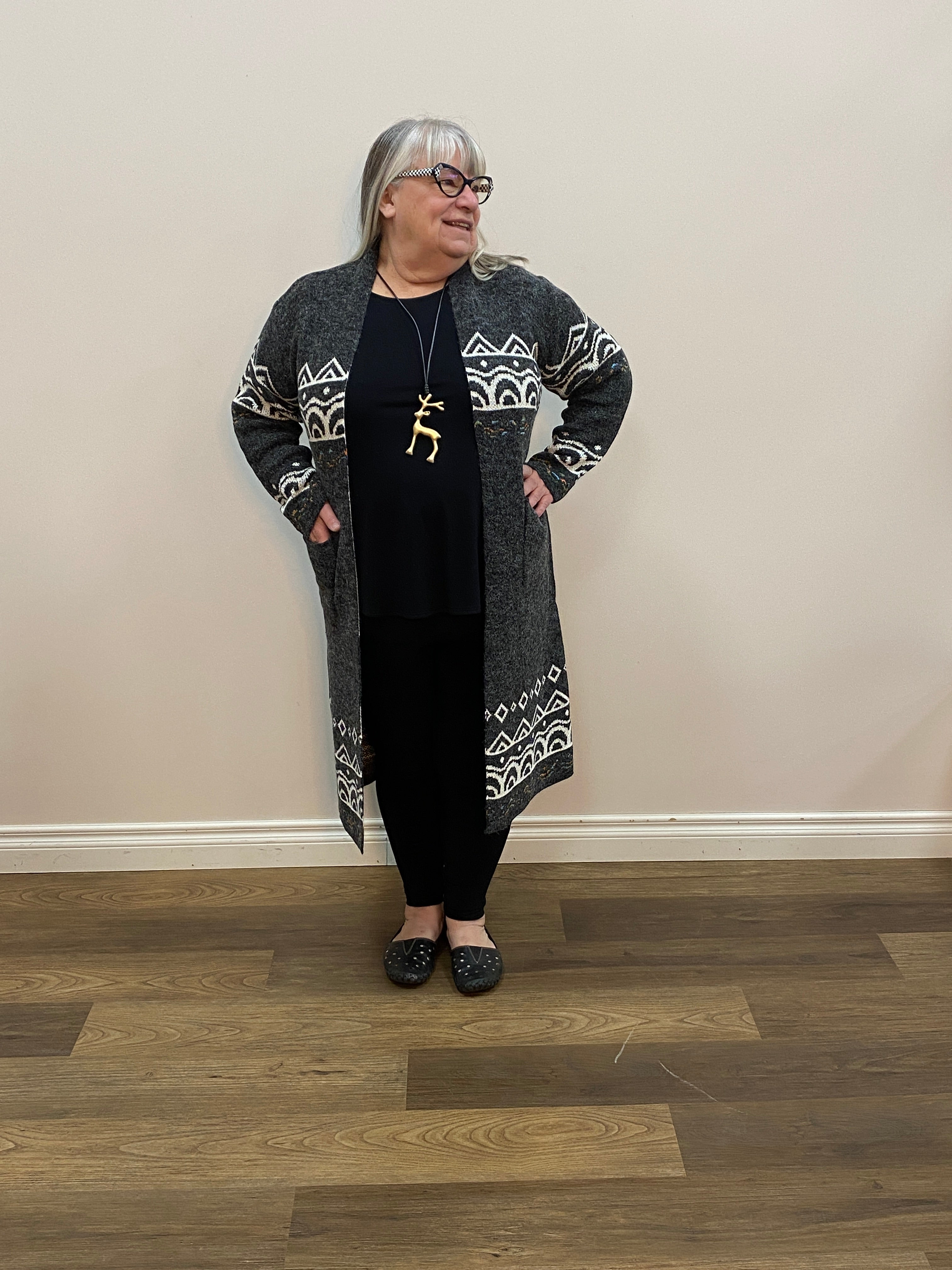 Person wearing a dark outfit with patterned sleeves standing in a room with wooden flooring.