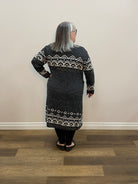 Person wearing a dark gray sweater with white patterns standing in a room with wooden flooring.