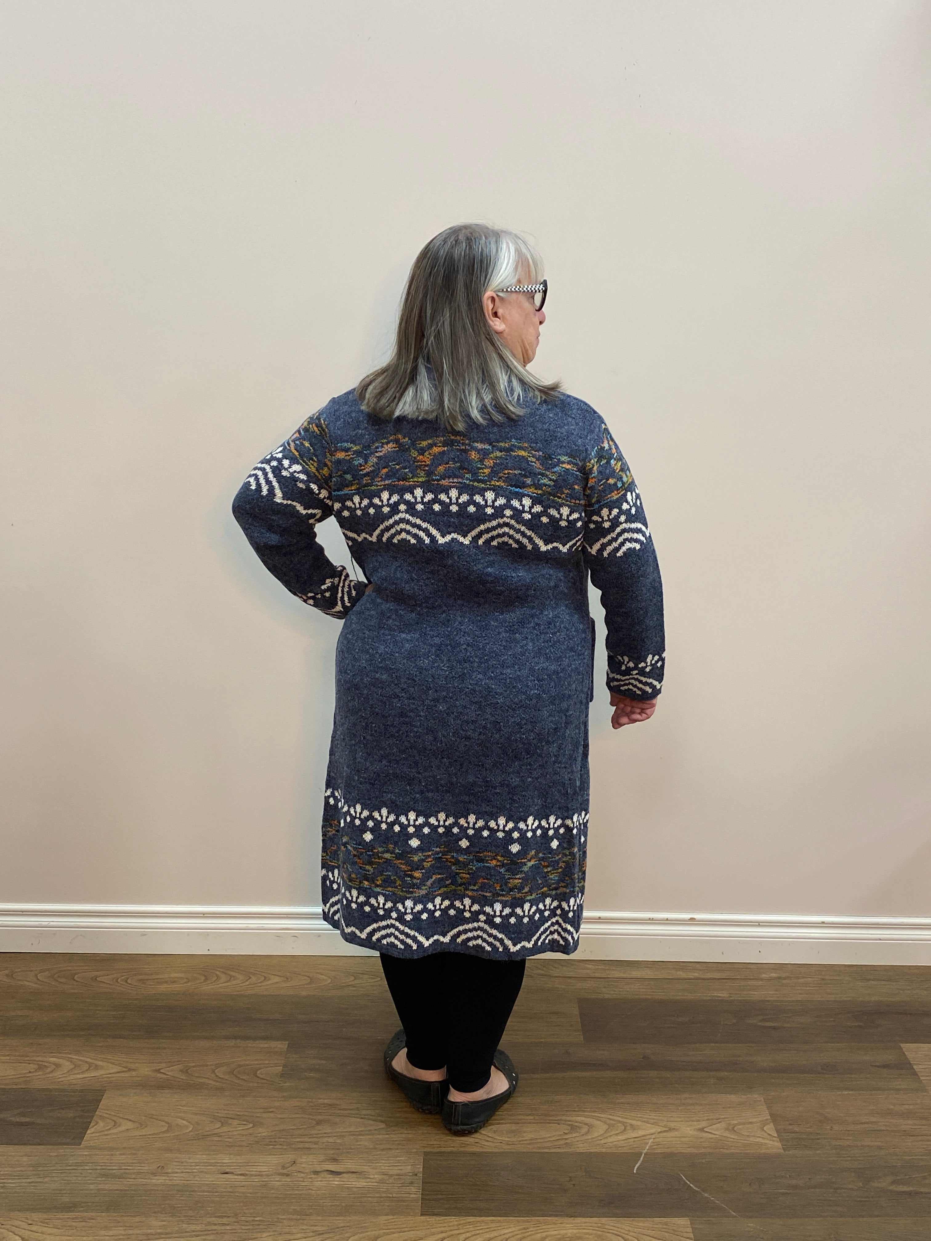 Person wearing a blue patterned sweater standing in room with a brown floor.