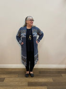 Person wearing a patterned outfit standing in a room with wooden flooring and a white wall.