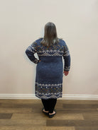 Person wearing a blue patterned jacket standing in a room with a brown floor.