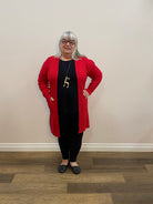 Person wearing a red cardigan and black pants standing on a wooden floor.