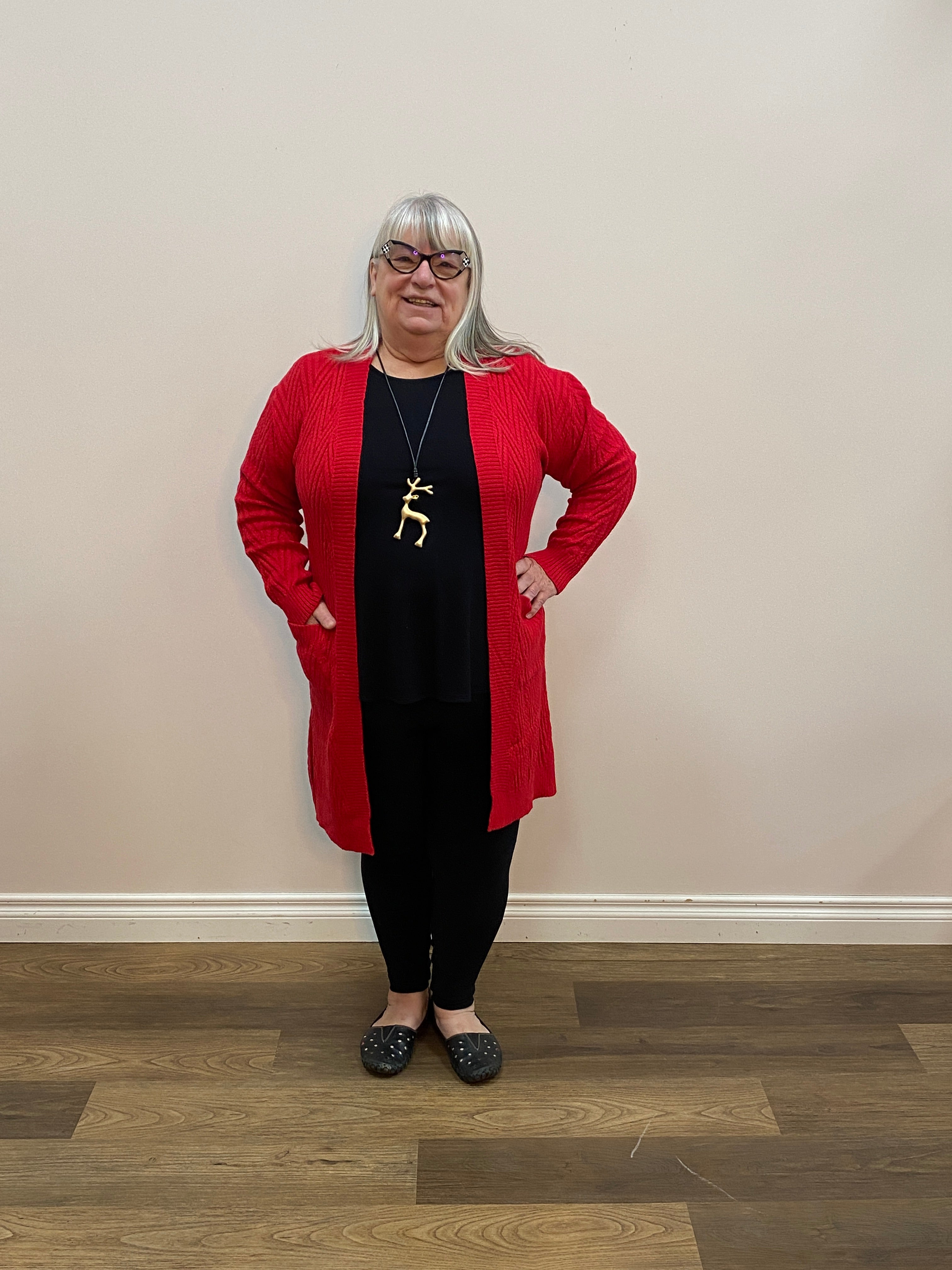 Person wearing a red cardigan and black pants standing on a wooden floor.
