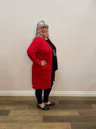 Person wearing a red sweater and black pants standing against a white wall with wooden floor.