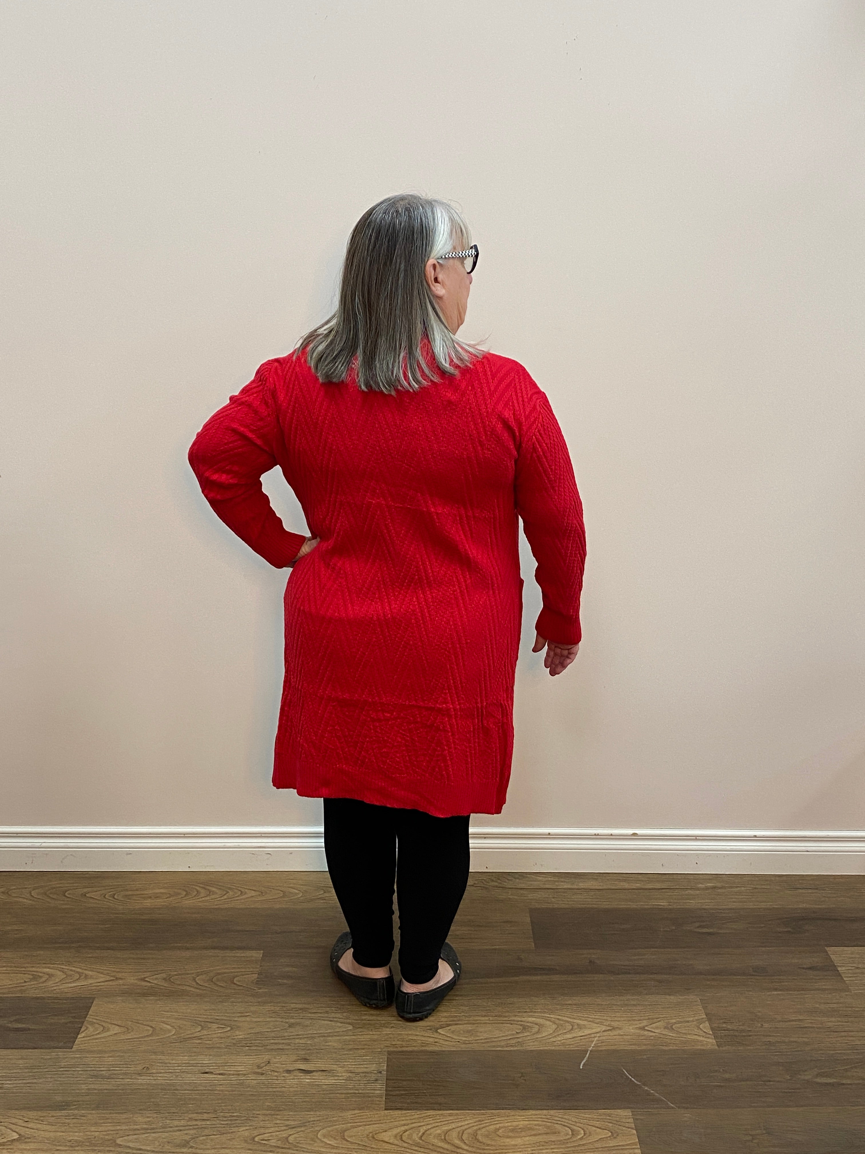 Person wearing a red sweater standing in a room with a wooden floor.