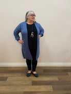 Person wearing a blue sweater and black pants standing in a room with wooden flooring.