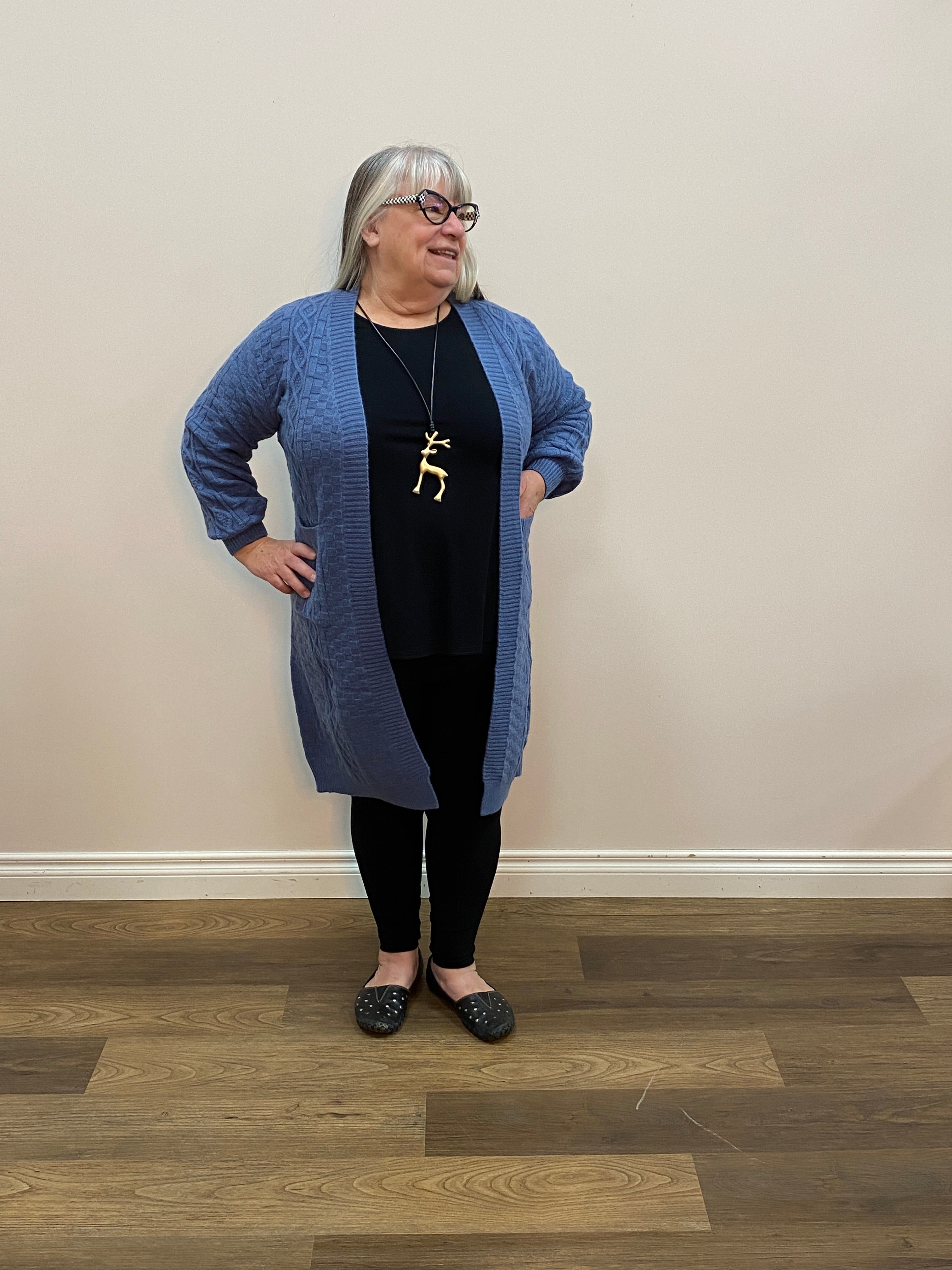 Person wearing a blue sweater and black pants standing in a room with wooden flooring.