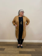 Person wearing a brown sweater and black pants standing in a room with wooden flooring.