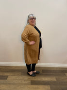 Person wearing a brown knitted cardigan in a room with wooden flooring and a white wall.