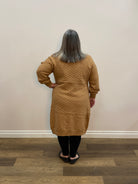 Person wearing a brown sweater standing against a white wall.