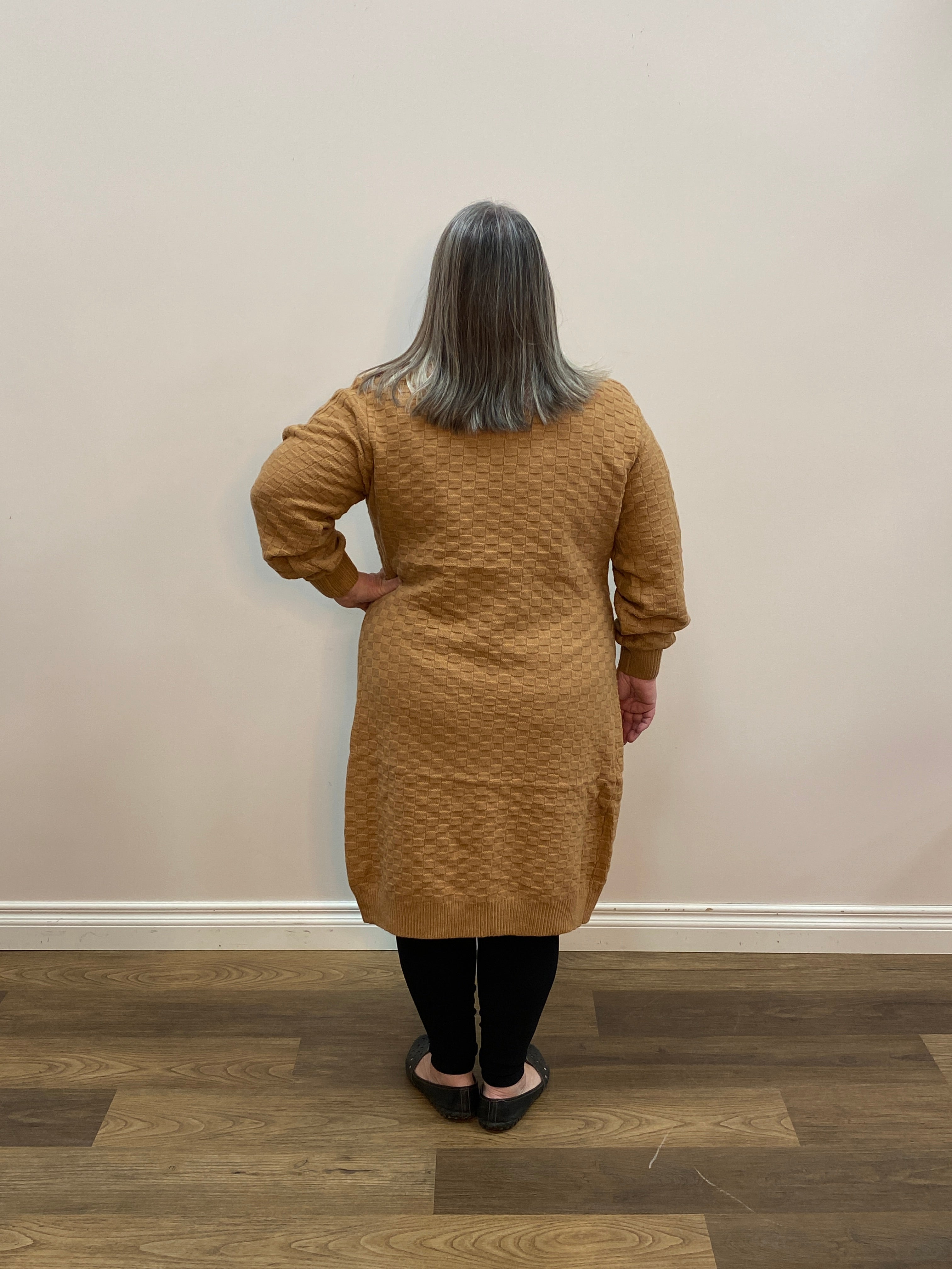 Person wearing a brown sweater standing against a white wall.